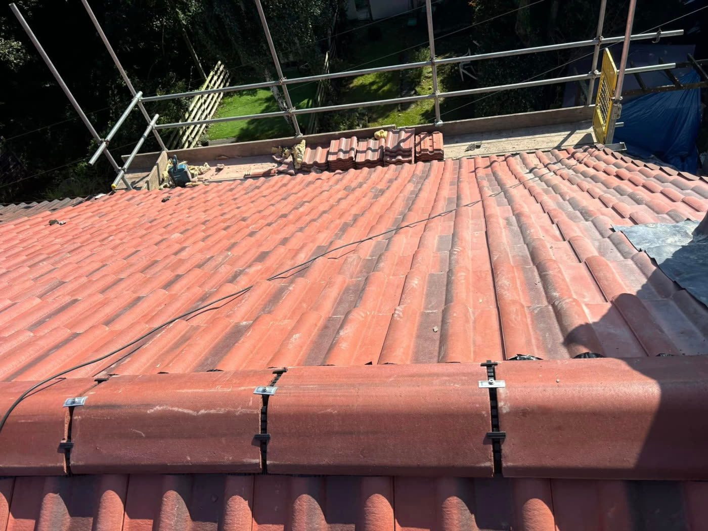 Dry ridge tiles mechanically clamped along the top of a red tiled roof during installation